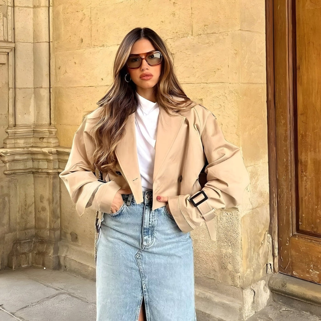 Frau im khakifarbenen Trenchcoat – moderner Look mit Sonnenbrille, weißem Oberteil und Jeansrock, perfekt für den Herbst